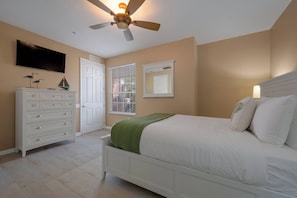 Quarto com cama, cômoda, televisão, ventilador de teto e janela com persianas.