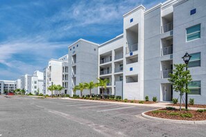 Um edifício residencial moderno, com várias andares, varandas, estacionamento e céu claro.