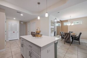 A kitchen with a central island, dining area with chairs, and a large mirror on the wall. - Sl4731-101 - 3BR Modern Apartment Storey Lake (Kissimmee)