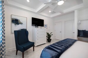 Ein Schlafzimmer mit einem Bett, einem Sessel, einem Schminktisch, einem Fernseher und einem Deckenventilator.