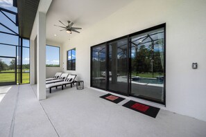 Ein moderner Außenbereich mit Sitzgelegenheit, Deckenventilator, großen Fenstern und Blick auf einen Swimmingpool.