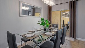 Un coin repas avec une table en verre, des chaises noires, un lustre, un miroir et une plante.