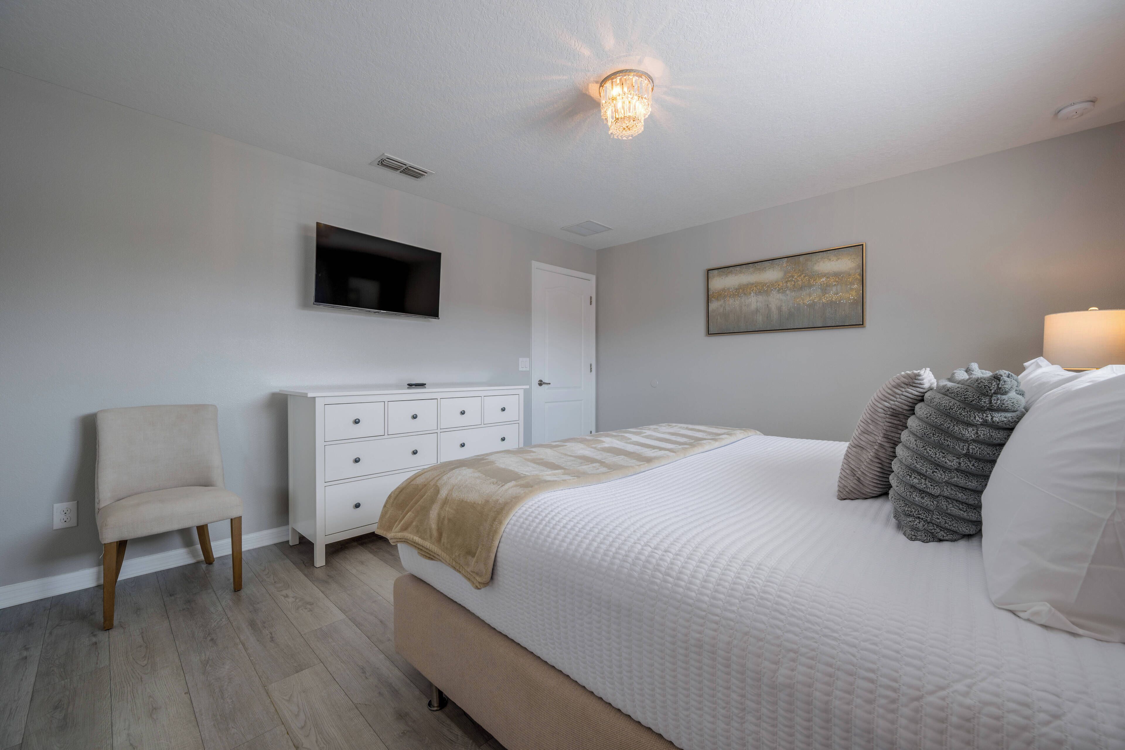 A bedroom with a bed, a chair, a dresser, a television, and a painting on the wall.