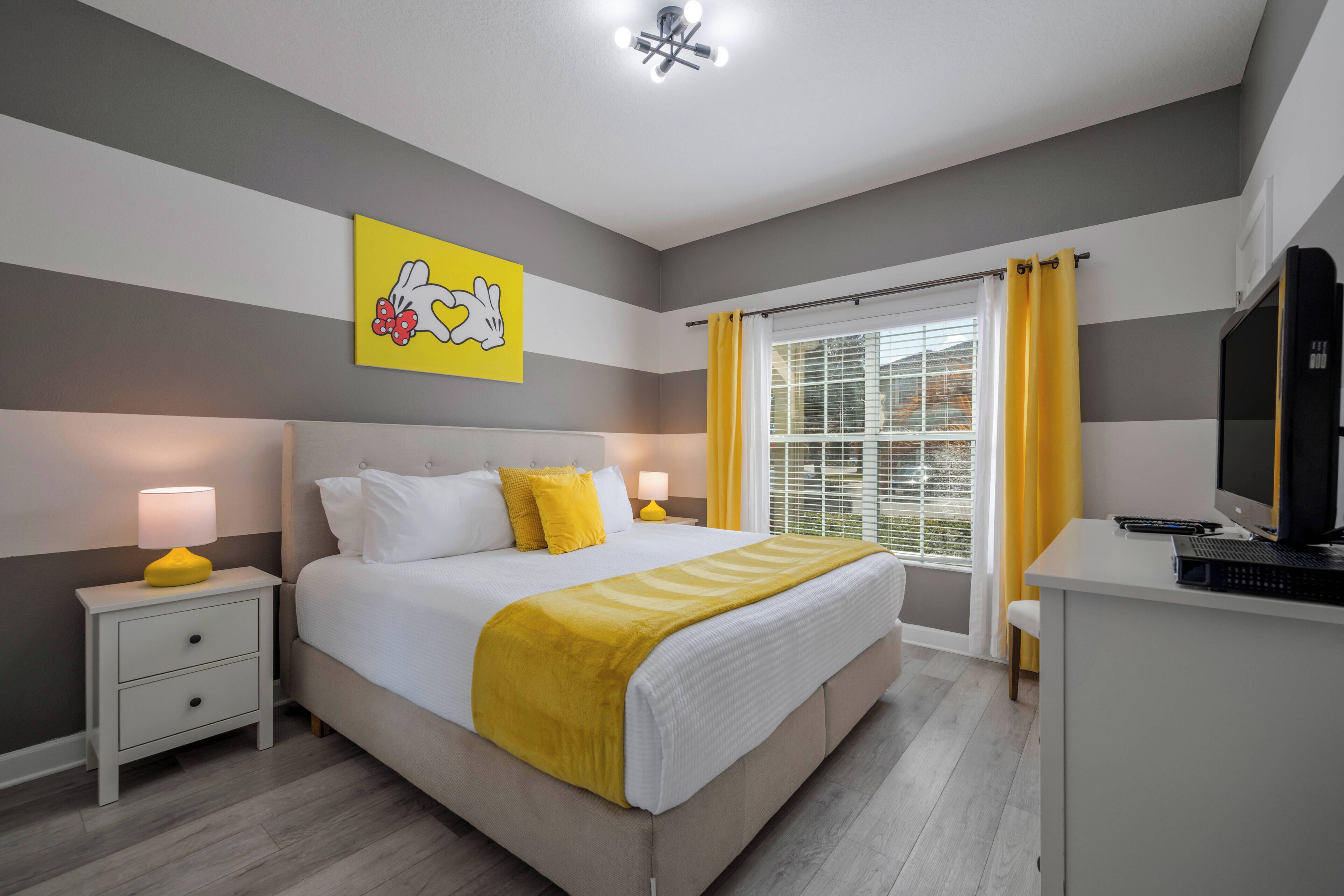 A bedroom with a bed, bedside tables, a desk, a television, and a window with curtains.
