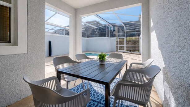 Un patio cubierto con una mesa y sillas, una piscina pequeña y vista a una casa a través de la estructura de vidrio.