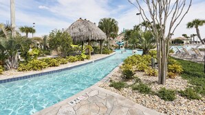 Una piscina con una estructura de techo de paja, rodeada de plantas tropicales y palmeras.