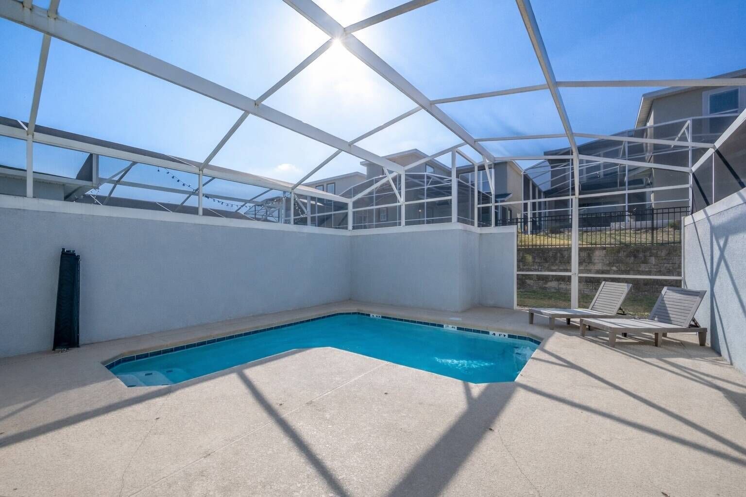 An indoor swimming pool with a clear view of the sky through a glass enclosure, surrounded by white walls and a concrete floor.