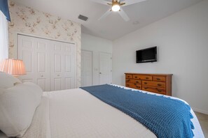 Ein Schlafzimmer mit Bett, Kommode, Fernseher und Deckenventilator.