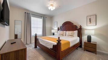 A bedroom with a wooden bed, a bedside table, a lamp, a TV mounted on the wall, and a window with curtains.