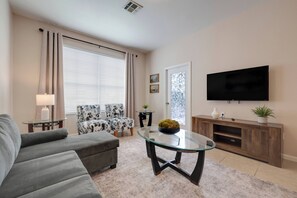 A living room with a sofa, two armchairs, a glass coffee table, a TV, a wooden entertainment unit, and a window with curtains. - Wp301 - 3BR Third Floor Condo - Windsor Palms (Kissimmee)