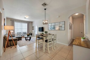 A modern living room with a sofa, a dining table with chairs, a TV, and a fireplace. - Wp301 - 3BR Third Floor Condo - Windsor Palms (Kissimmee)