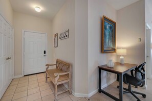A hallway with a wooden bench, a desk with a chair, a painting, and a door. - Wp301 - 3BR Third Floor Condo - Windsor Palms (Kissimmee)