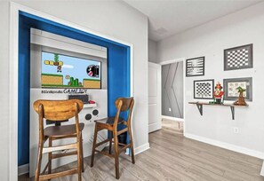 A room with a Nintendo Game Boy II, two wooden chairs, and chessboard decorations on the wall. - Sl4895 - 5BR House With Pool Near Disney Area (Kissimmee)