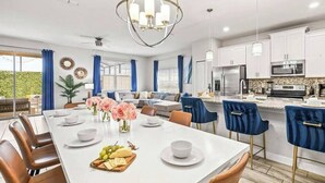 Una cocina moderna con armarios blancos, una isla central y un comedor con mesa y sillas blancas.