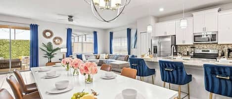 A modern kitchen with white cabinets, a central island, and a dining area with a white table and chairs.