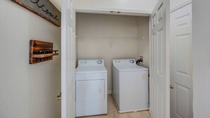A laundry room with two white front-loading washers and dryers, a wooden rack with hanging clothes, and a 'Welcome' sign on the wall. - Wp302 - 2BR Condo Near Walt Disney World (Kissimmee)