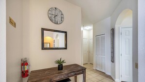 A hallway with a wooden console table, a fire extinguisher, a clock, and a mirror. - Wp302 - 2BR Condo Near Walt Disney World (Kissimmee)