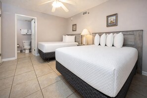 Ein Hotelzimmer mit einem großen Bett, zwei Einzelbetten, einem Badezimmer und einem Deckenventilator.