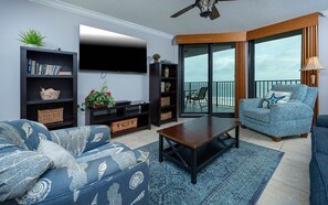 Un salon comprenant un canapé, une table basse, une bibliothèque, un téléviseur à écran plat et un balcon avec vue.