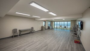 A spacious room with a long table and chairs, a television mounted on the wall, and large windows offering a view of the ocean. - Phoenix Iii 3043 1 Bedroom Condo (Orange Beach)