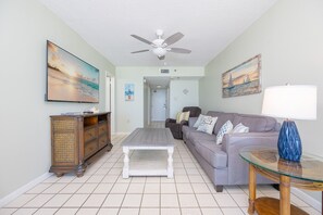 Ein Wohnzimmer mit Deckenventilator, Flachbildfernseher, Sofa, Couchtisch und Lampe.