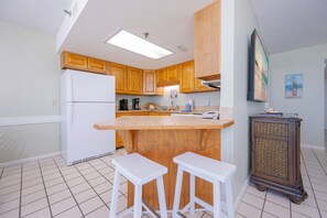 Eine Küche mit Holzschränken, einem weißen Kühlschrank, einer zentralen Kochinsel mit Hockern und einem dekorativen Schrank.