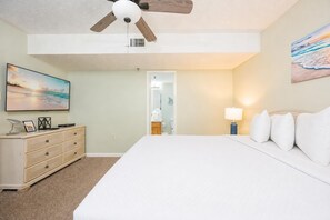 Ein Schlafzimmer mit einem Bett, einem Schminktisch, einem Deckenventilator, einem Gemälde und einer Lampe.