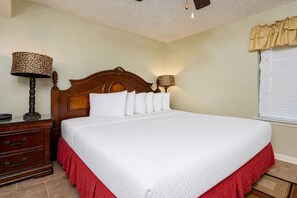 A neatly made bed with a wooden headboard, a bedside table with a lamp, and a window with blinds. - Phoenix Iii 3033 1 Bedroom Condo (Orange Beach)