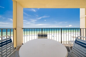 A balcony with a white table and chairs, overlooking a beach with clear blue water and a few people in the distance. - Phoenix Iii 3085 1 Bedroom Condo (Orange Beach)