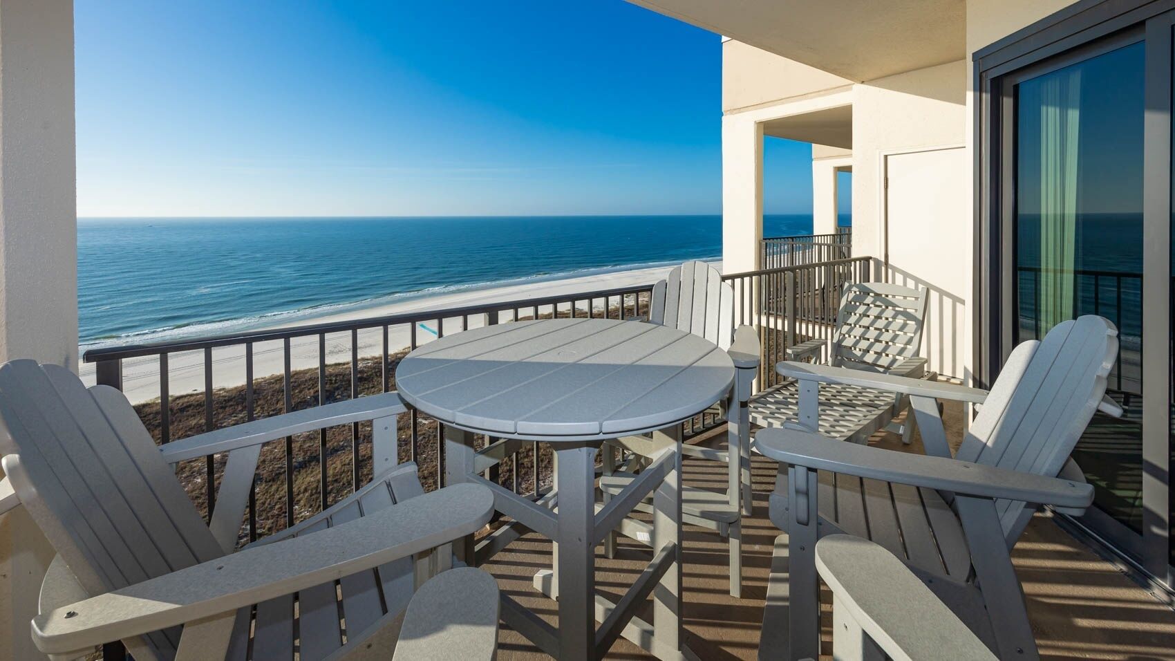 Ein Balkon mit Tisch und Stühlen, mit Blick auf Strand und Meer.