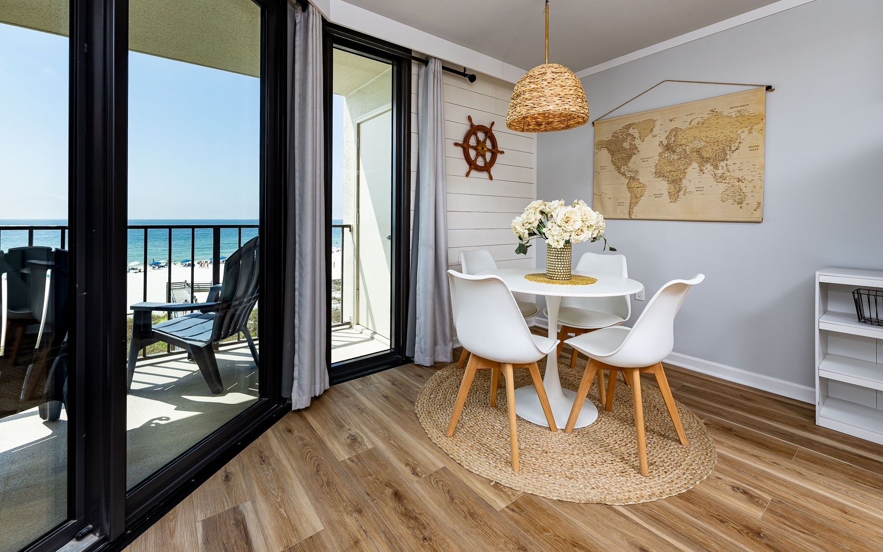 Un balcon donnant sur la plage, une table ronde avec des chaises, une carte du monde accrochée au mur et un décor représentant un gouvernail de navire.
