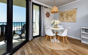 A balcony with a view of the beach, a round table with chairs, a world map on the wall, and a ship's wheel decoration. - Phoenix Iii 3035 1 Bedroom Condo (Orange Beach)