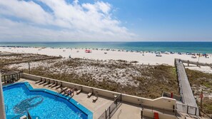 A beach view with a pool area, lounge chairs, and a wooden deck. - Phoenix Iii 3035 1 Bedroom Condo (Orange Beach)