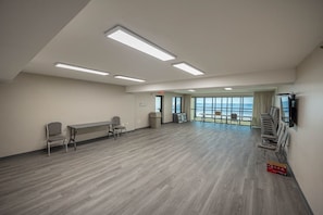 Una habitación amplia con una mesa larga y sillas, un televisor montado en la pared y grandes ventanas con vistas al océano.