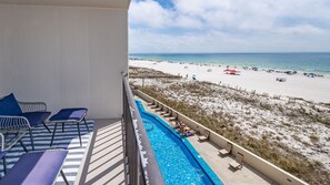 A balcony with a pool, lounge chairs, and a view of a beach with umbrellas. - Phoenix Iii 3035 1 Bedroom Condo (Orange Beach)