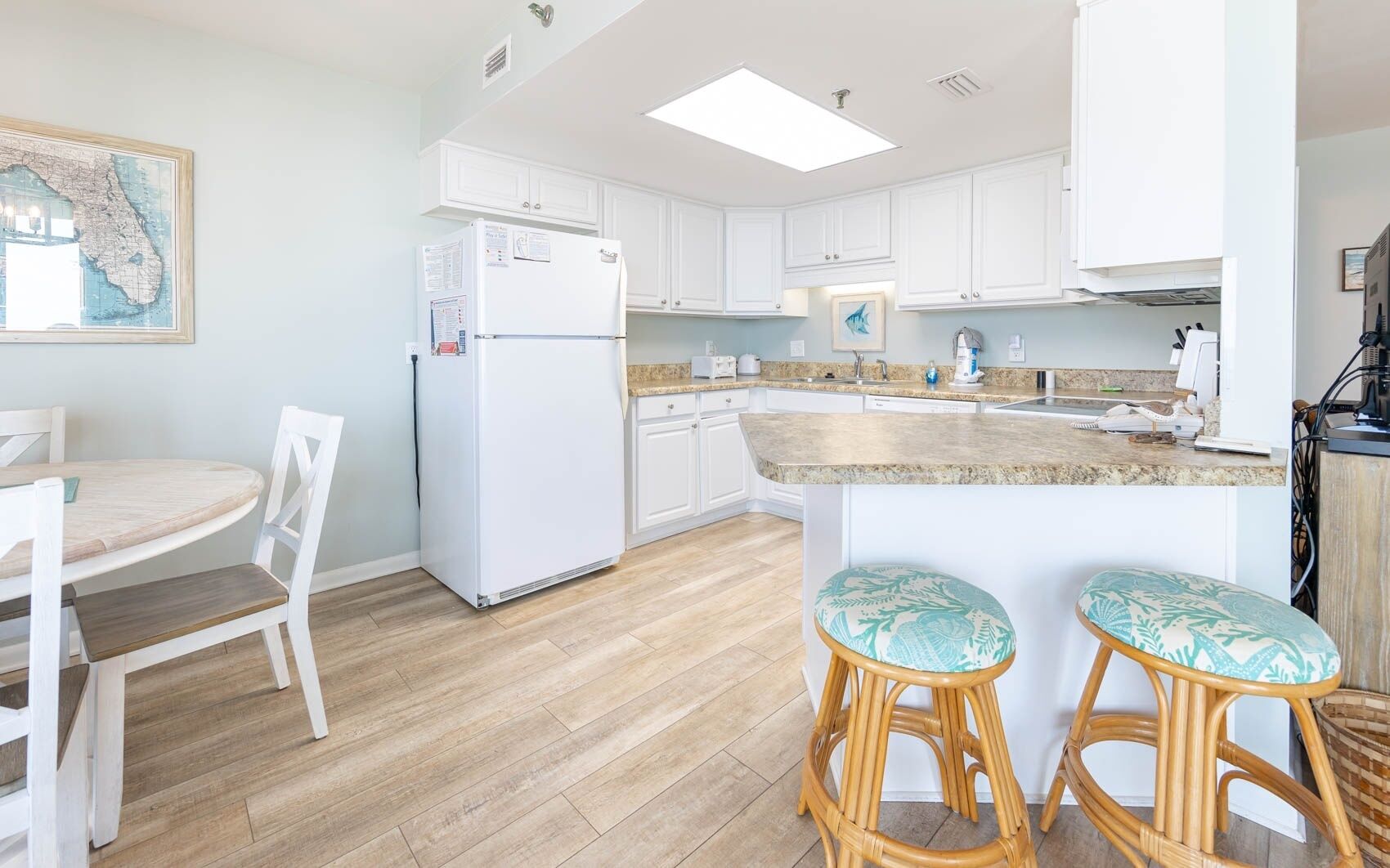A kitchen with white cabinets, a refrigerator, a dining table with chairs, and a bar area with stools.