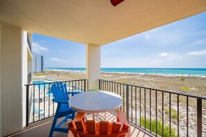 Un balcon avec vue sur la plage et l’océan, un espace piscine et des sièges extérieurs.