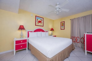 Ein Hotelzimmer mit einem Bett, zwei Nachttischen mit Lampen, einem Deckenventilator und einem Vorhangfenster.