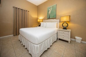 A bedroom with a large bed, two bedside tables with lamps, a painting on the wall, and a curtain on the window. - Phoenix Vii 7103 3 Bedroom Condo (Orange Beach)