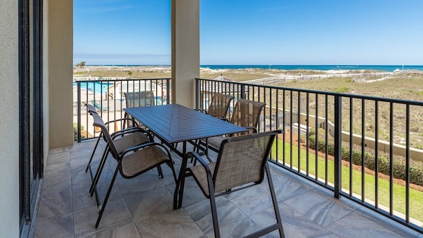 A balcony with a table and chairs, overlooking a beach and pool area. - Phoenix Vii 7103 3 Bedroom Condo (Orange Beach)