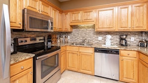 A kitchen with wooden cabinets, a microwave, a stove, a dishwasher, and a coffee maker. - Phoenix Vii 7103 3 Bedroom Condo (Orange Beach)