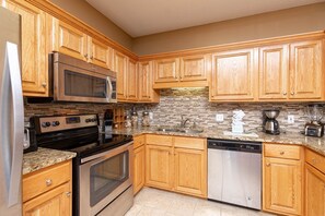 A kitchen with wooden cabinets, a microwave, a stove, a dishwasher, and a coffee maker. - Phoenix Vii 7103 3 Bedroom Condo (Orange Beach)