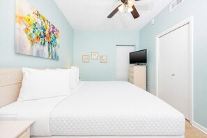 Une chambre à coucher avec un lit, un ventilateur de plafond, une télévision et une porte.