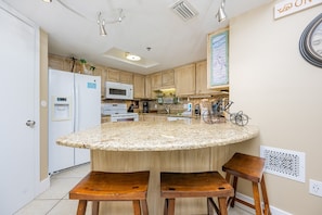 A kitchen with a central island, wooden chairs, a microwave, and a water dispenser. - Phoenix Vii 71010 2 Bedroom Condo (Orange Beach)