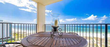 A round table with a candle centerpiece on a balcony overlooking a beach.