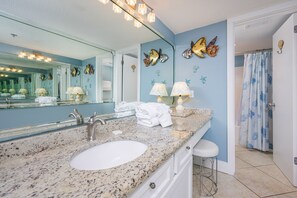 Une salle de bain avec un comptoir en granit, un lavabo, un miroir et des coquillages décoratifs accrochés au mur.