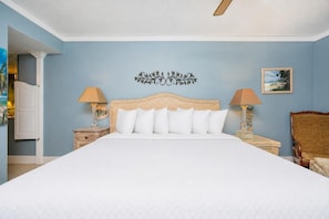 A bedroom with a large bed, two bedside tables, a wall-mounted artwork, and a chair. - Phoenix Vii 71010 2 Bedroom Condo (Orange Beach)