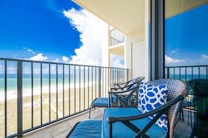 A balcony with a view of a beach, equipped with two chairs and a table. - Phoenix Vii 71010 2 Bedroom Condo (Orange Beach)