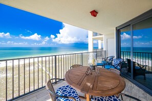 Un balcon avec une table et des chaises en bois, donnant sur une plage et l’océan.