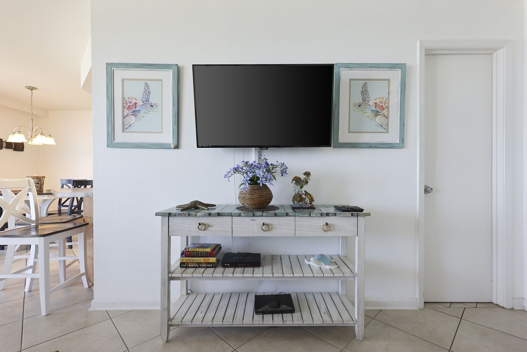 Una consola blanca con un televisor de pantalla plana encima, flanqueada por dos cuadros enmarcados.